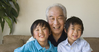 A grandfather smiles with two grandsons on his lap equally as happy.