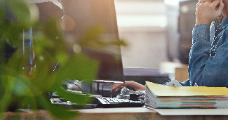 A woman working at her desk with a stack of papers next to her.